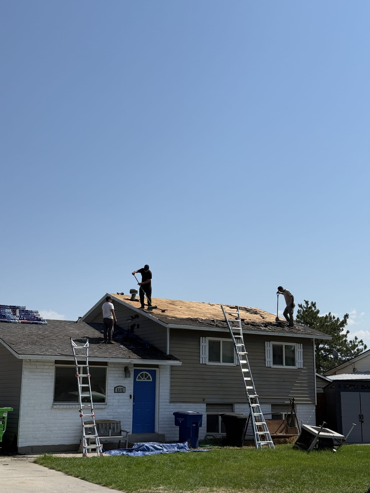 Workers on residential roof with old shingles and metal roof frame