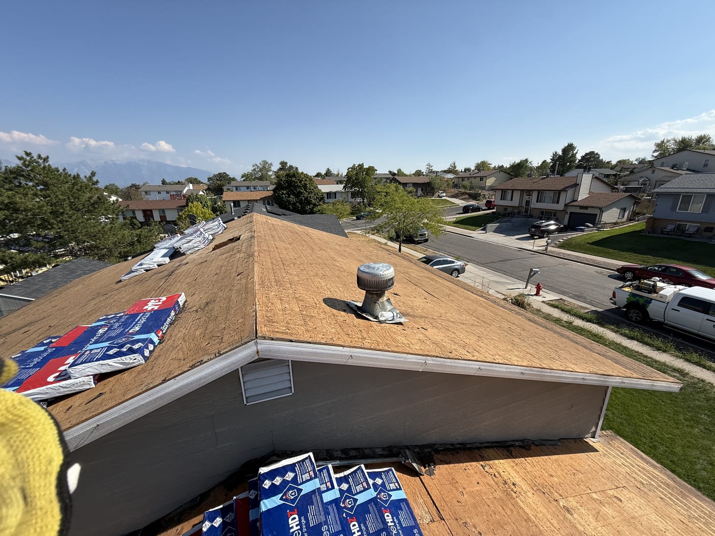 View of bare OSB roof corner with roof vent and stacked GAF materials, in-progress re-roof