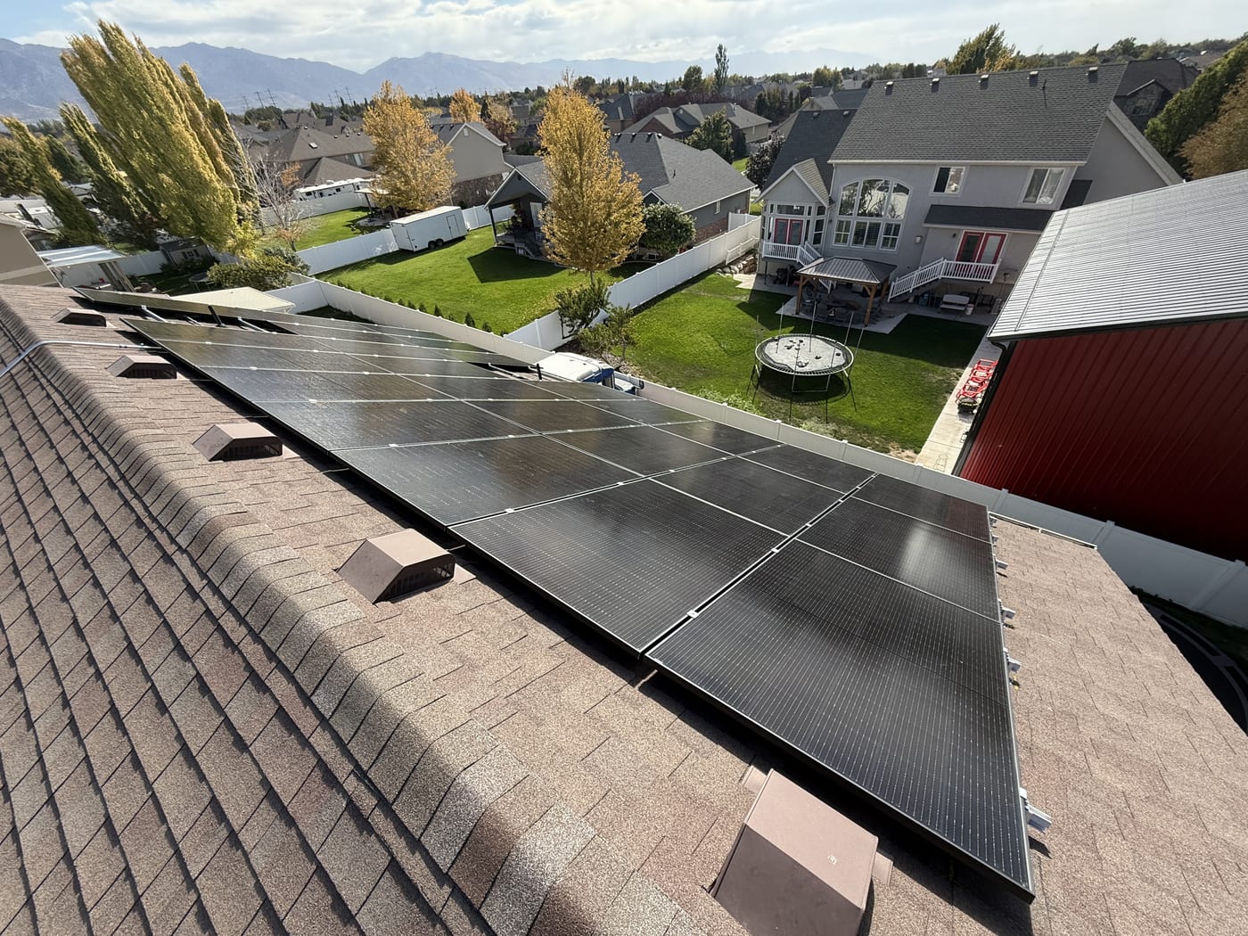 [Trina panels] Drone aerial view of completed solar array on residential shingle roof with neighborhood visible below, no snow present