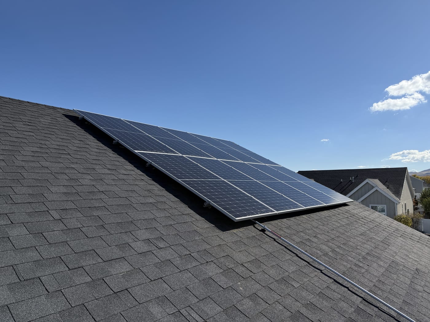 Sideways shot of solar panels at edge of gray shingle roof with blue sky