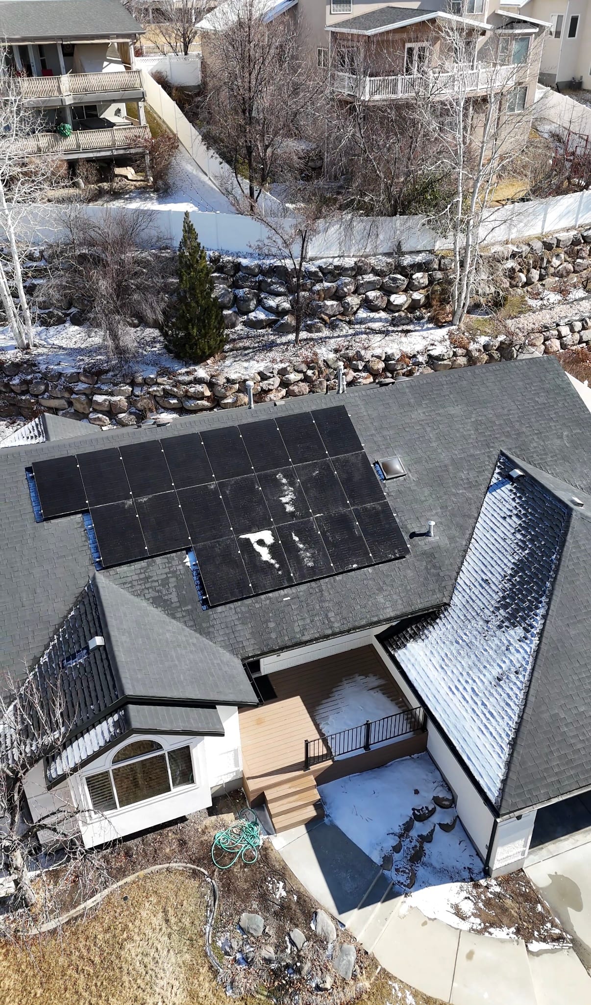 [black-on-black Trina panels] Drone aerial looking down at residential rooftop solar installation with snowy yard and neighboring properties visible