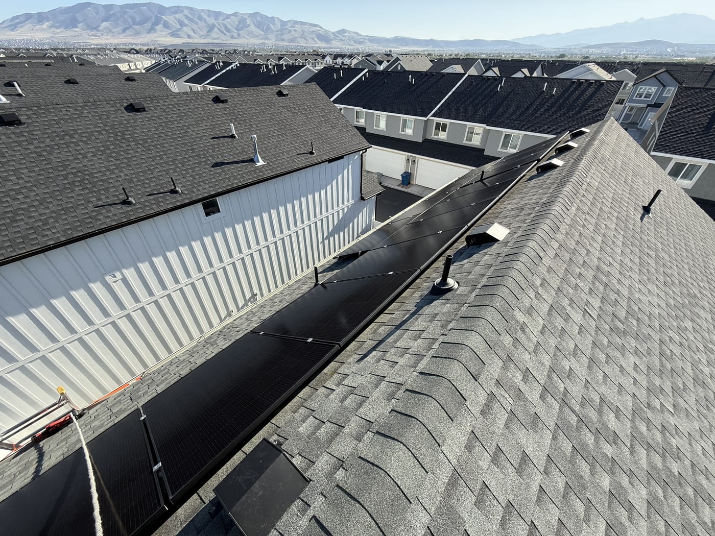 Racking rails and panels on gray shingle roof with neighborhood visible