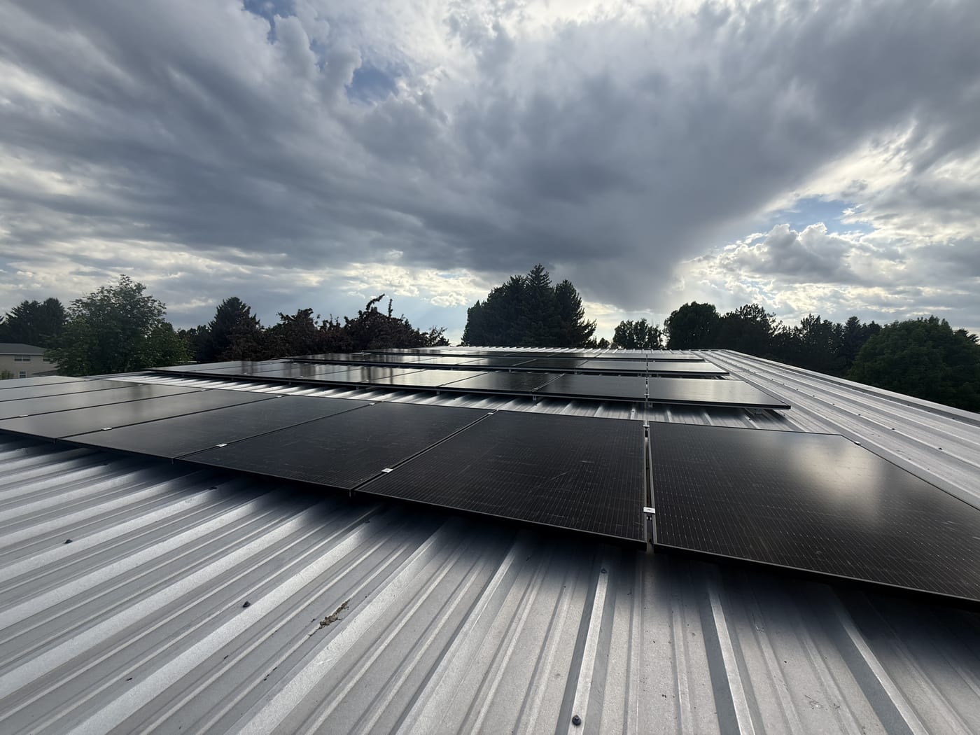 Completed solar panel array on metal standing seam roof with cloudy sky and trees in background