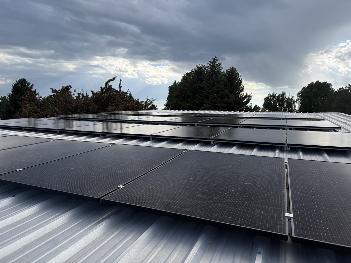 Solar panels installed on metal roof with dramatic cloudy sky and tree line backdrop