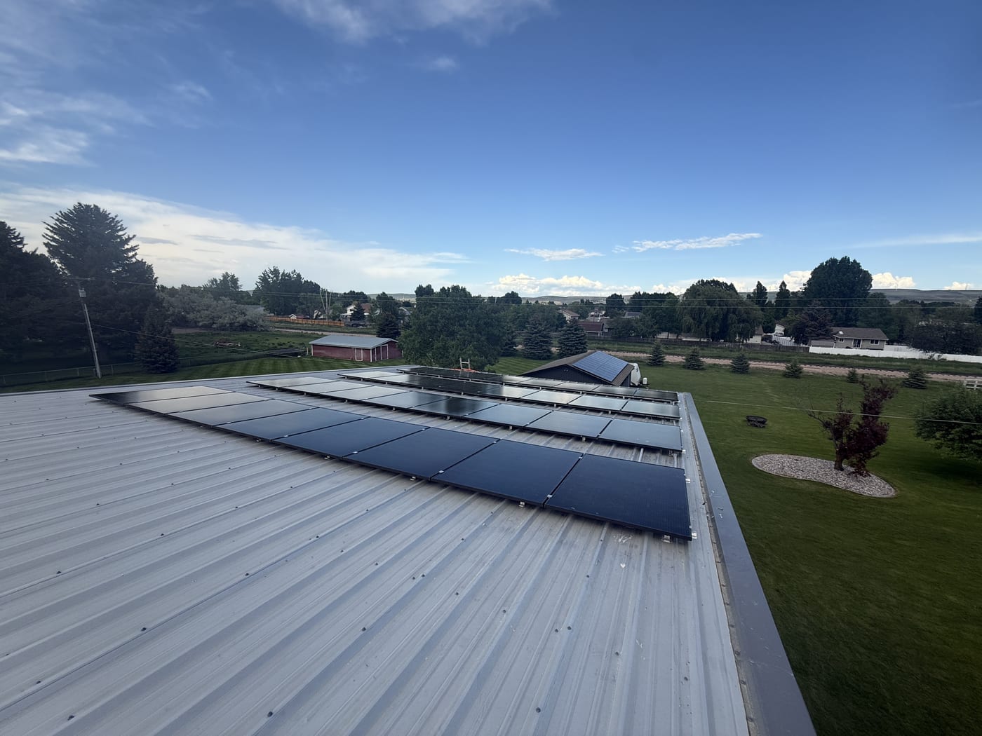 Solar array on metal roof overlooking green fields and rural landscape with blue sky