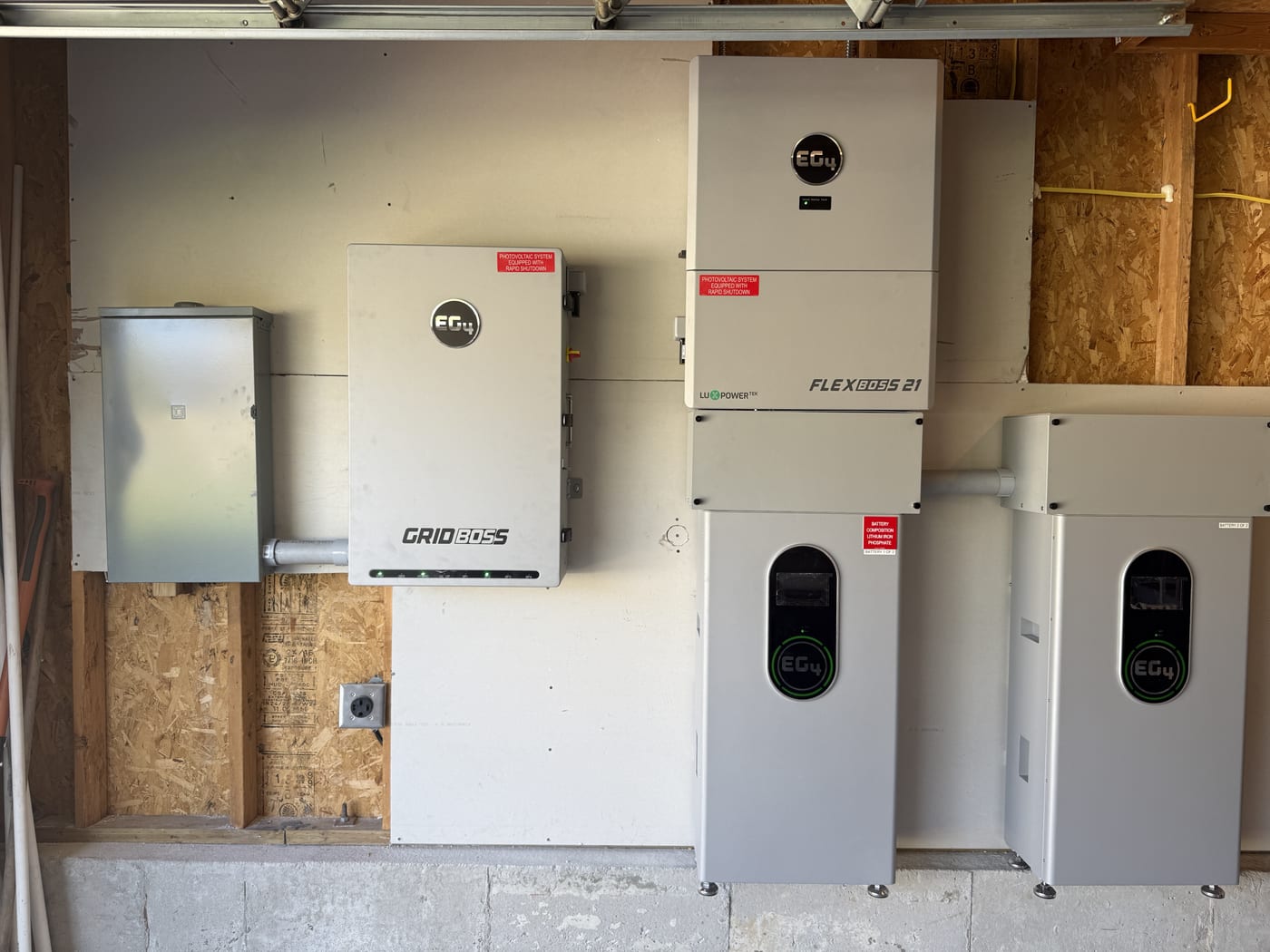 EG4 GridBOSS with FlexBOSS 21 and two battery units showing active charge status on garage wall