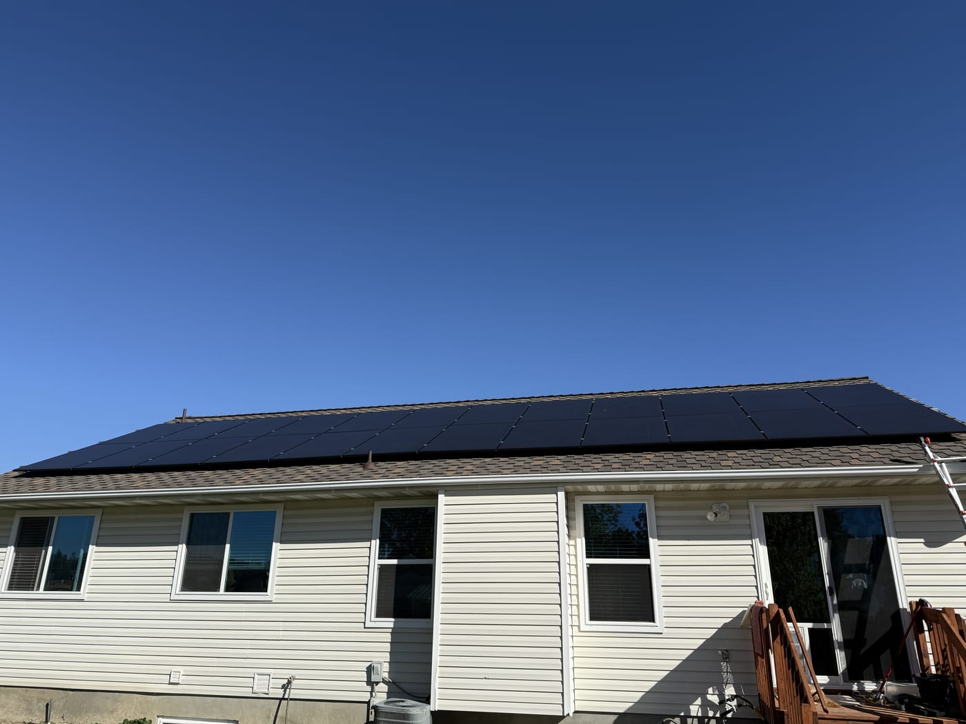 [Trina panels] House rear exterior showing full solar array on roof with white siding and blue sky