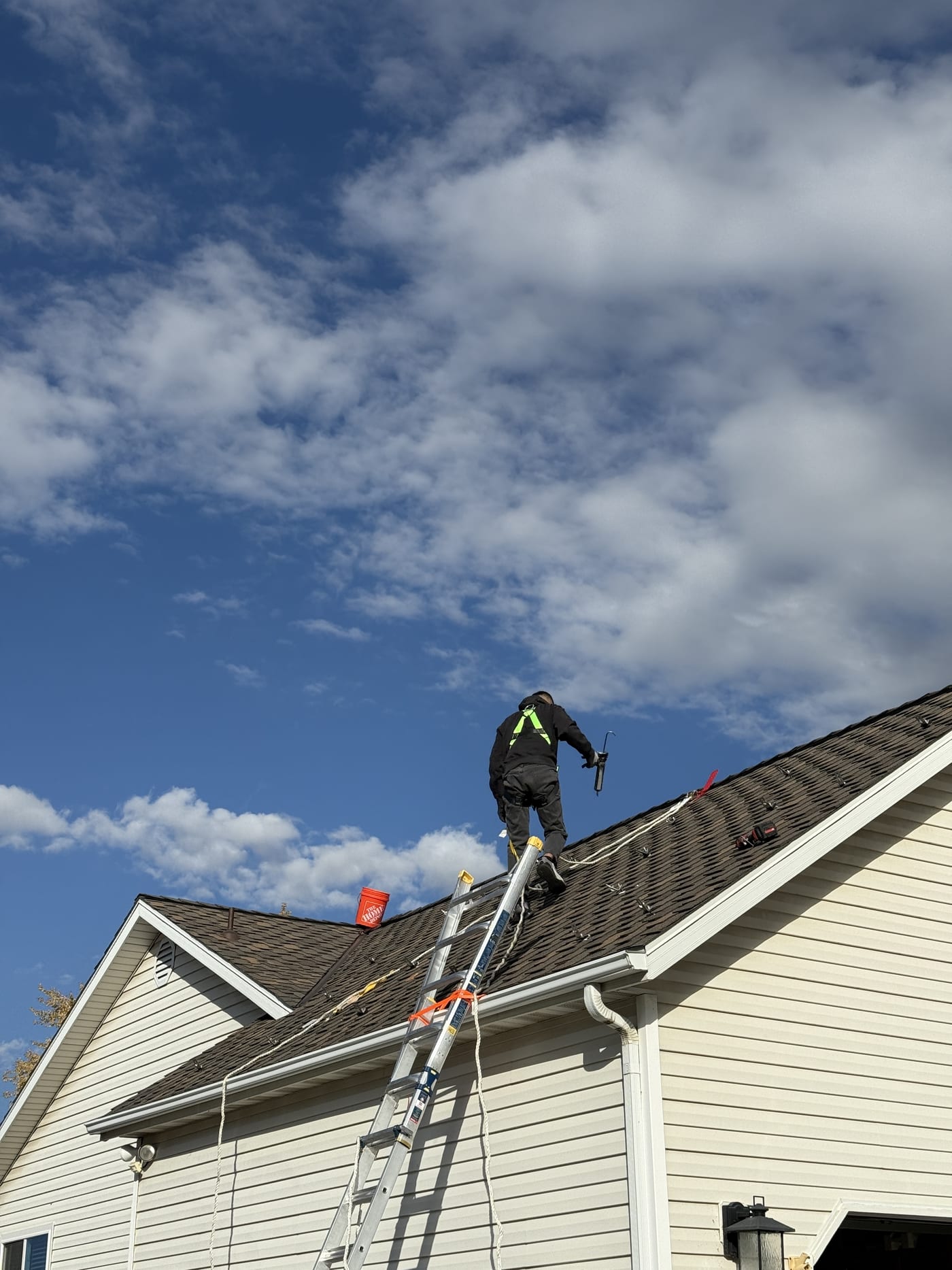 Installer with safety gear working on steep roof with ladder visible and dramatic cloudy sky