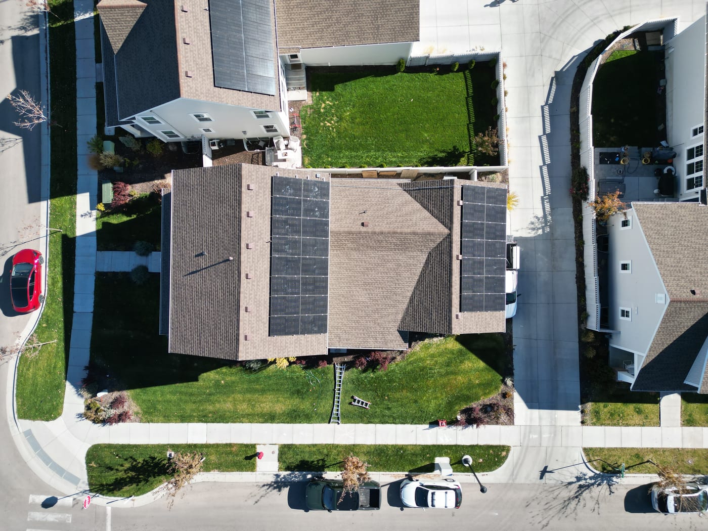Wide drone aerial view of solar installation on residential roof with suburban neighborhood and streets