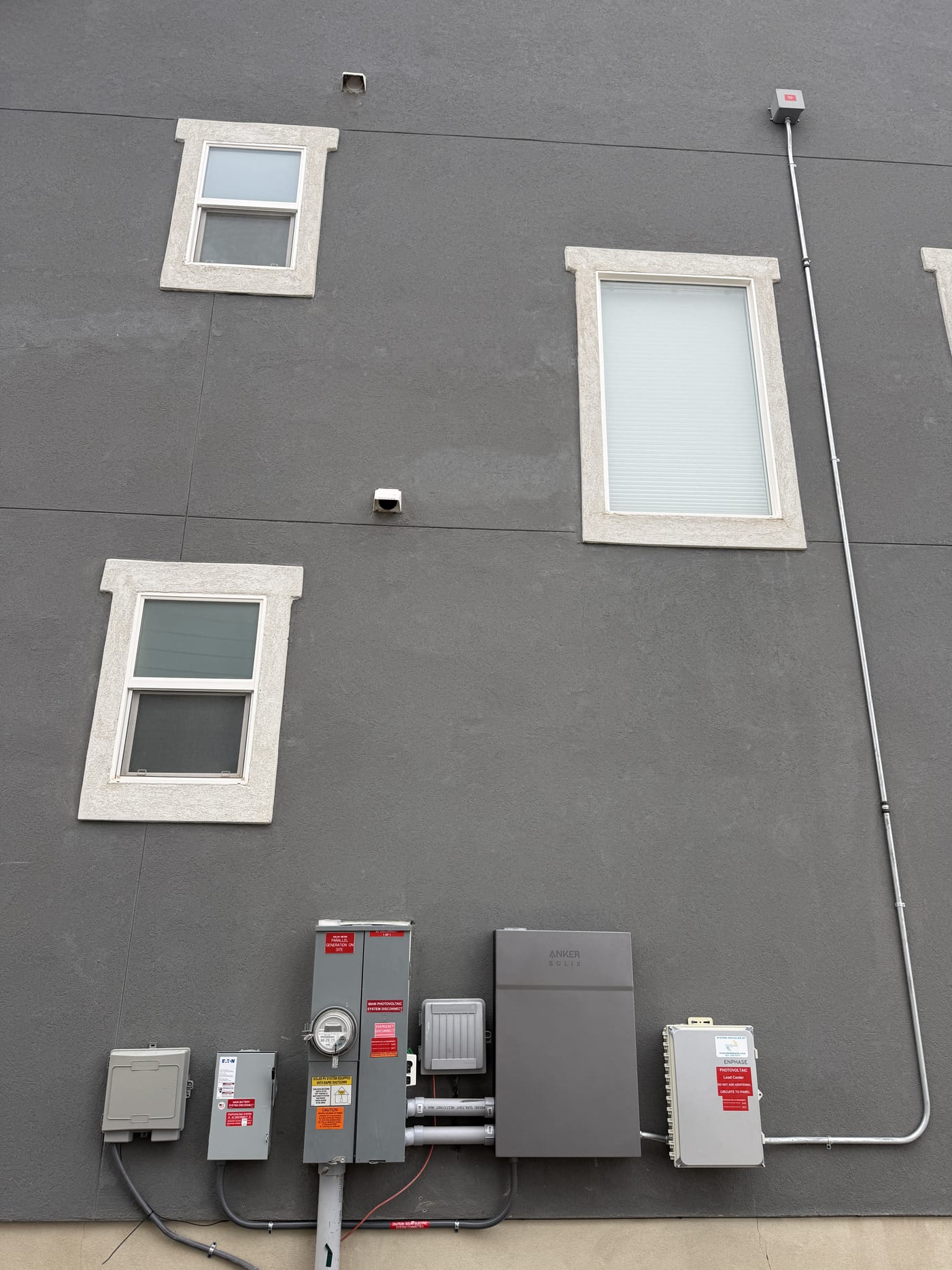 Wide view of house exterior showing conduit run to electrical equipment with windows on gray stucco