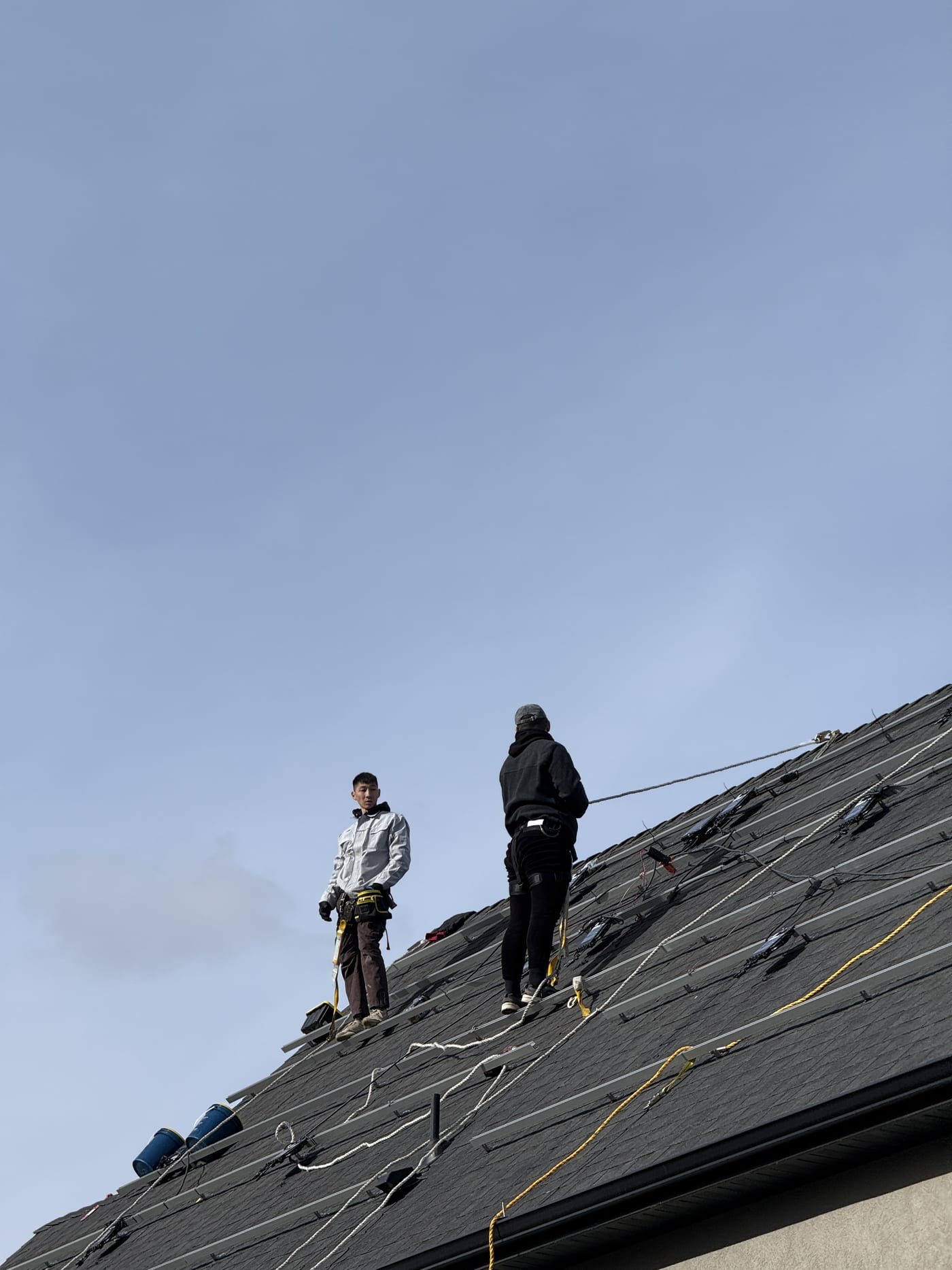 Two crew members on roof working with racking and wiring, close-up from roof level