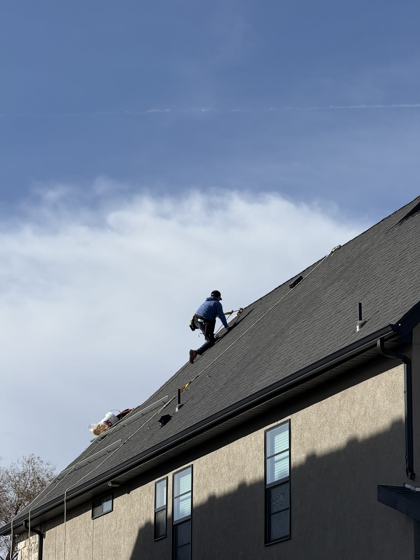 House exterior showing crew on dark shingle roof, neighborhood homes and mountains visible