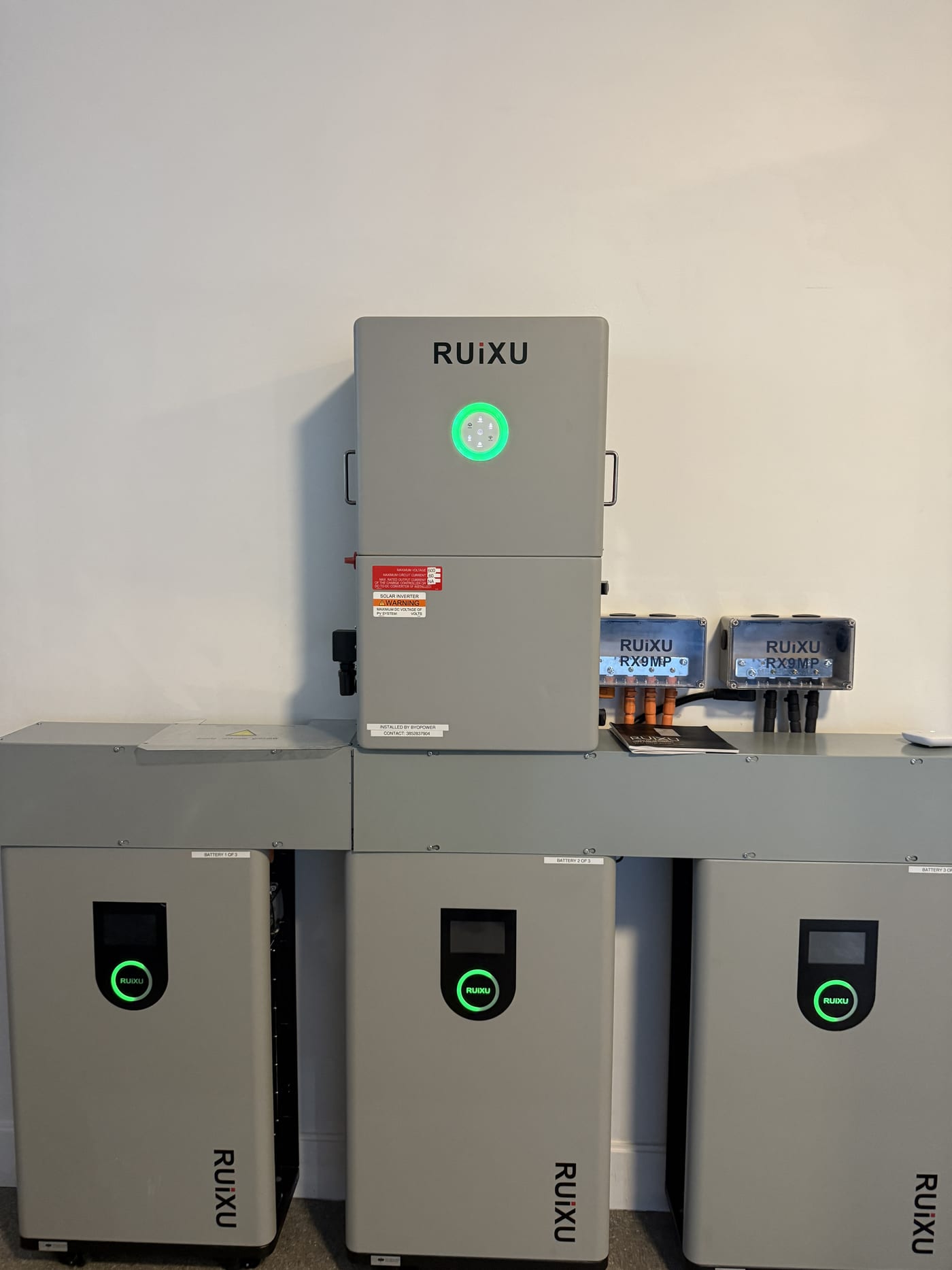 RUiXU inverter and 3 battery units wall-mounted, close-up showing brand logos, green status LEDs, and RX9MP junction boxes with wiring