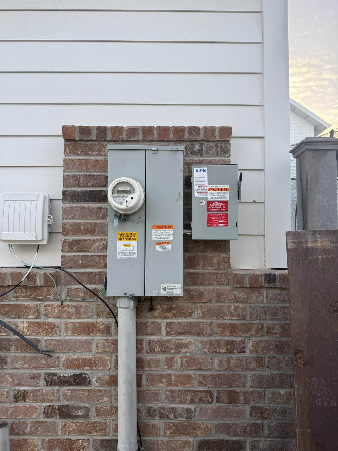 Electrical equipment on exterior brick and siding wall showing Eaton disconnect, meter socket, electrical panel, and conduit runs (image rotated sideways)